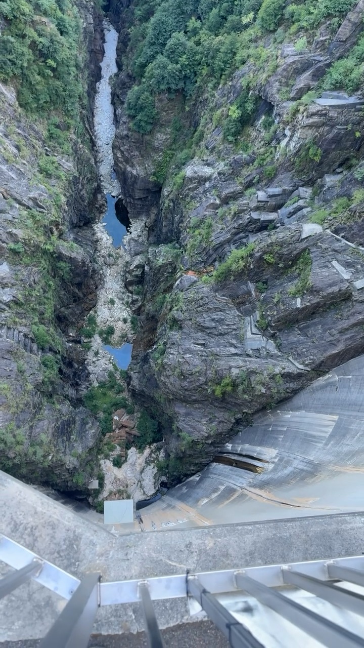 Senkrechter Blick über das Geländer der Staumauer hinunter in die Schlucht, ganz unten das Flussbett.