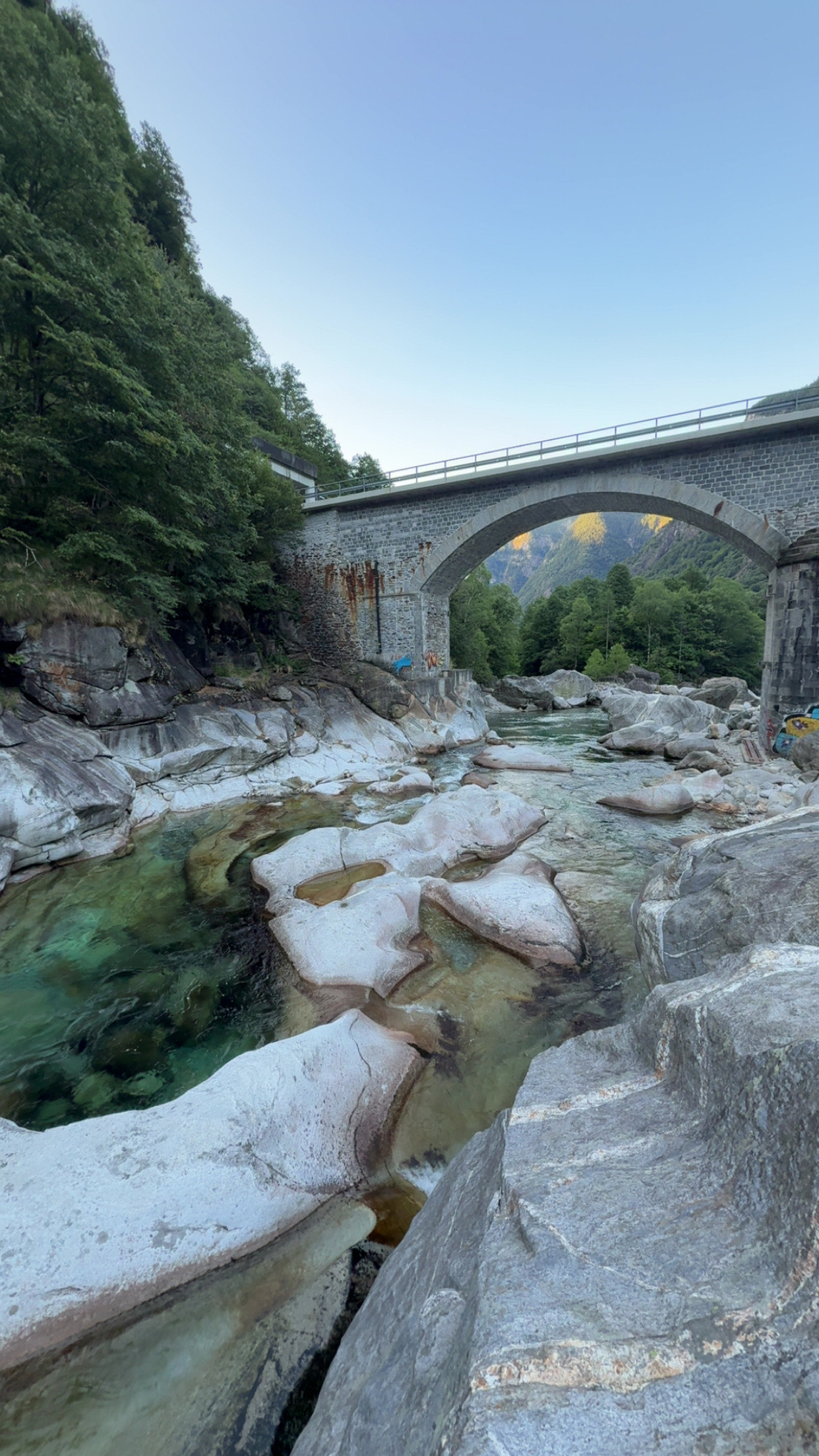 Weisser Granit und türkisgrünes Wasser unter einer Steinbogenbrücke in der Verzasca.