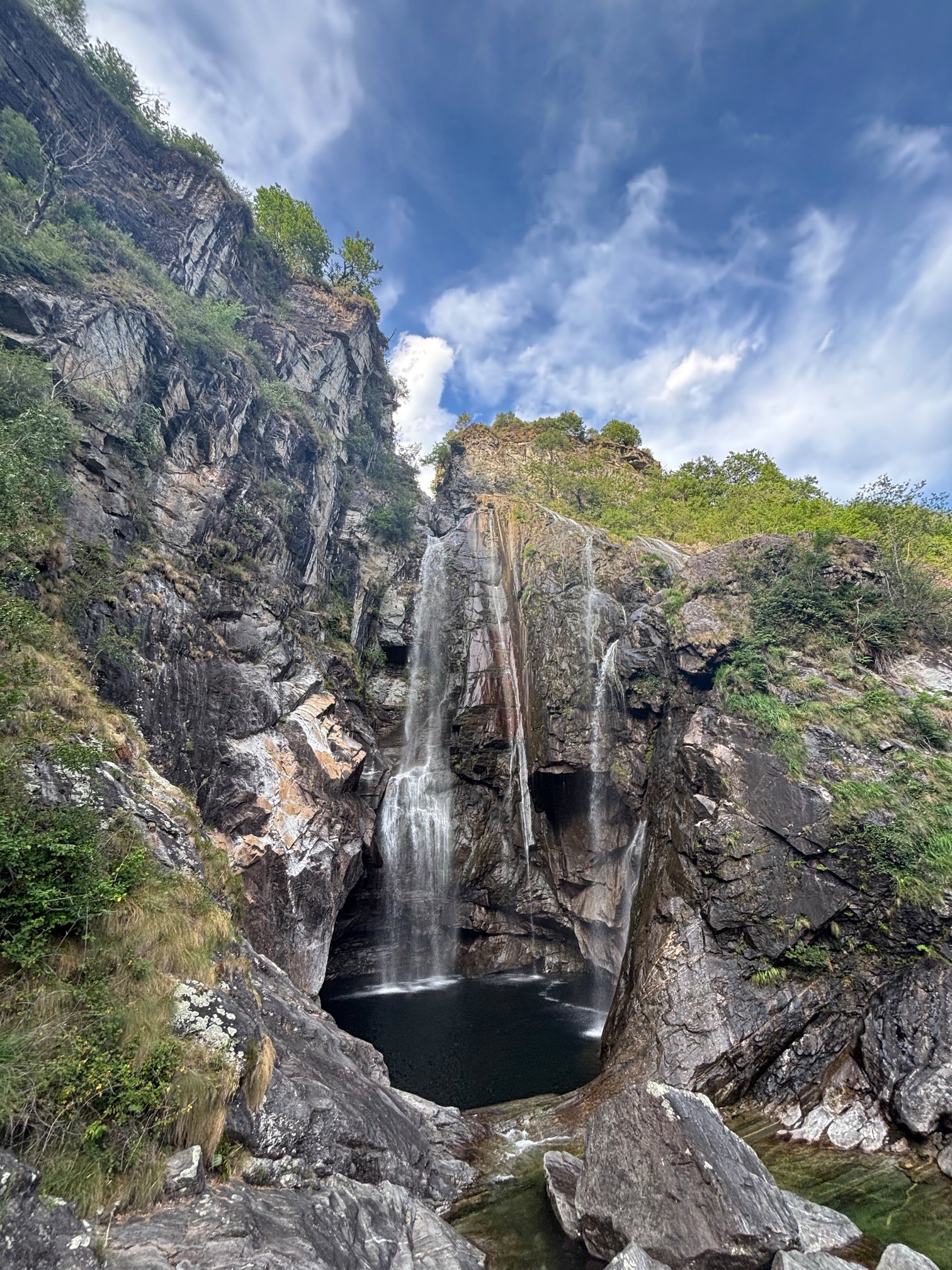 Ein Wasserfall stürzt in zwei Strängen über dunklen Fels in ein rundes, tiefes Becken.